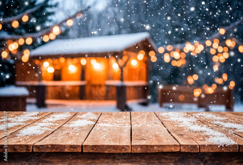 Empty wooden table covered with snow on a defocused background of a winter gazebo with garlands