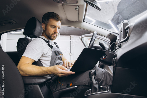 Automotive mechanic running diagnostics software on computer. Mechanic sitting in car and working on laptop while doing vehicle diagnostic test in auto service garage.