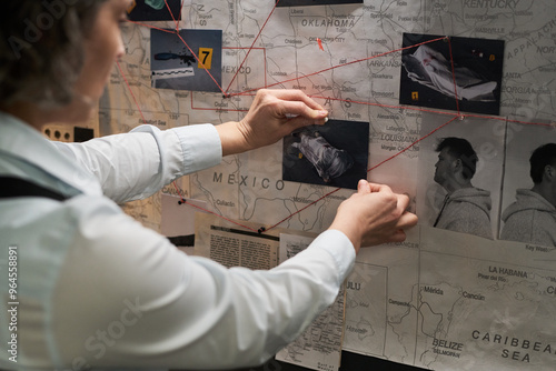 Investigative professional analyzing a detailed board with photographs, red string connections showing connections and evidence linking various places and people together