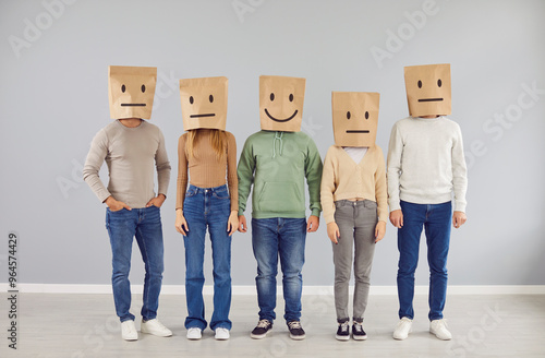 Happy smiley sanguine social man and group of apathetic phlegmatic indifferent people standing by grey wall background wearing brown shopping bags on heads with different drawn emoji mood expressions