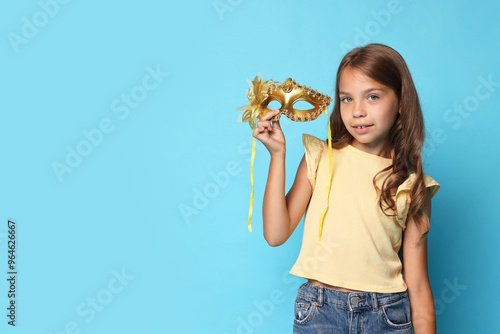 Cute girl with carnival mask on light blue background. Space for text