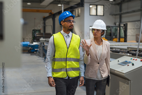 Indian female factory manager introducing the production line to a recruit, an African American worker, and congratulating him on a new job, front view.