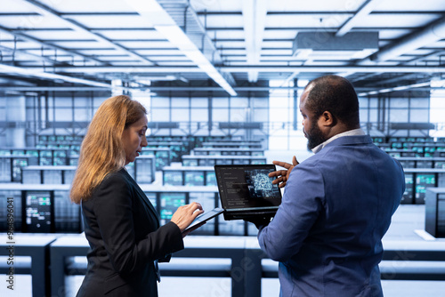 Teamworking colleagues using AI software on laptop, programming in AI data center. IT staff members in high tech server hub facility upgrading artificial intelligence systems