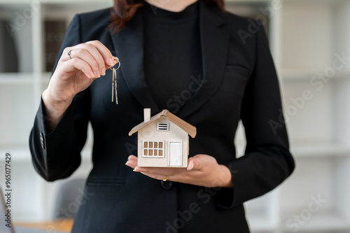 A real estate agent standing in the office, holding house keys and a house model.