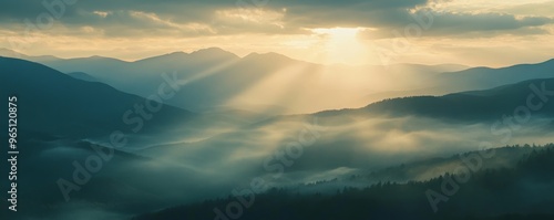 Sunrise over misty mountain range with sun rays, serene landscape