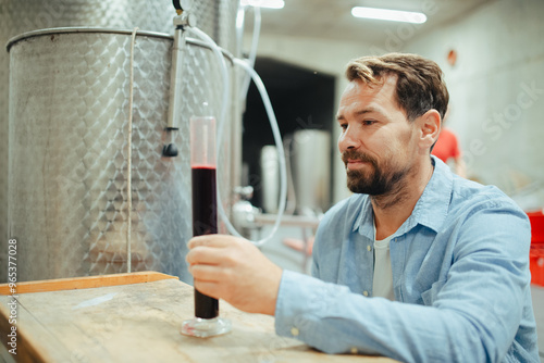 Winemaker standing in the wine cellar, controlling, testing wine sample.