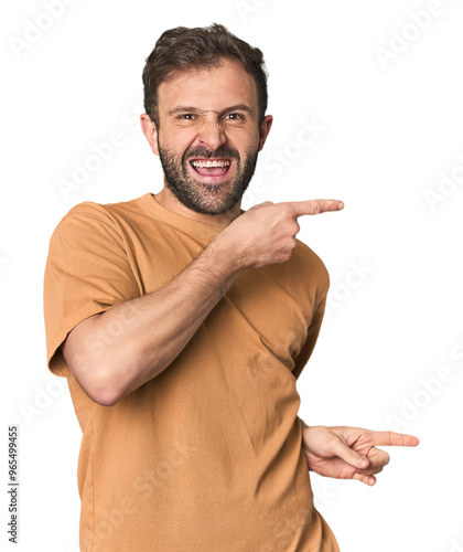 Studio portrait of young Hispanic male pointing with forefingers to a copy space, expressing excitement and desire.