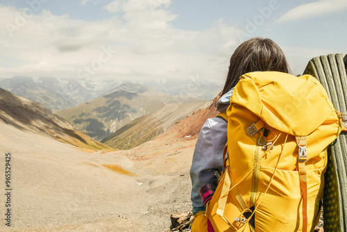 Close up view from the back unrecognizable woman with yellow stylish backpack with flask sticking out of the side pocket. Mock up copy space banner. Woman watch mountains valley in sunny day