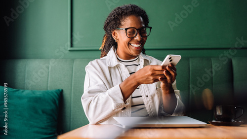 Black woman smiling while using smartphone in cafe