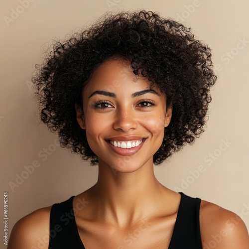 closeup portrait of black softly smiling woman is 35 years old with curly hair on beige background