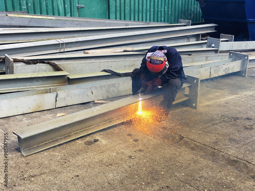 A worker using an electric plasma cutter to reduce the size of a steel girder