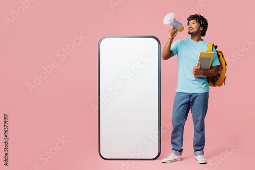 Full body young Indian boy student wear blue casual clothes backpack bag hold books big huge blank screen mobile cell phone scream in megaphone isolated on plain pink background. High school concept.