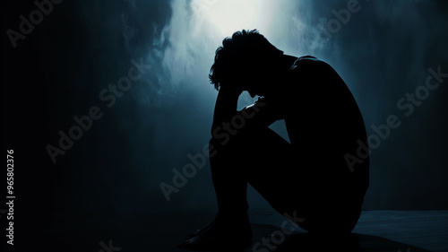 Silhouette of a depressed man sitting with head in hands conveying a sense of deep sadness and depression