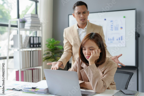 Businessman angrily criticizing a female colleague working on laptop in the office