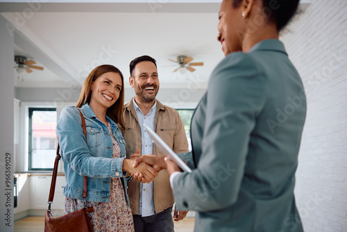 Happy woman shaking hands with real estate agent while buy new home with her husband.