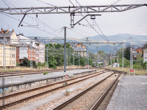 View of the end of the platform at Ponferrada train station on its way out towards the mountains where the low signals are illuminated in red under the wires of the catenary