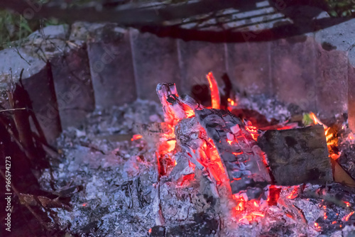 Rozżarzone drewno w dogasającym ogniu na rodzinnym pikniku. Ognisko wieczorem ze stalowym rusztem do opiekania (grillowania) zawieszonym nad nim.