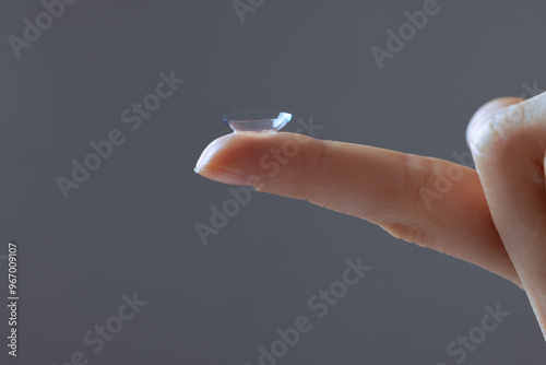 Close-up of finger holding contact lens, on grey background, concept of poor eyesight, astigmatism, myopia, hyperopia, treatment of deteriorating vision