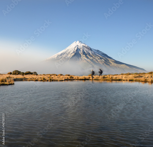 Couple hiking Pouakai circuit. Snow-capped Mt Taranaki in the background. New Zealand.