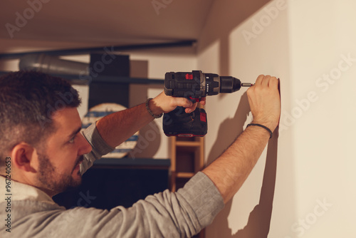 Handyman with battery drill fixing kitchen cabinets and shelf.