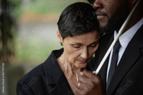 Portrait of sorrowful senior woman grieving over loss of loved one leaning on comforting man during memorial ceremony at gravesite, copy space