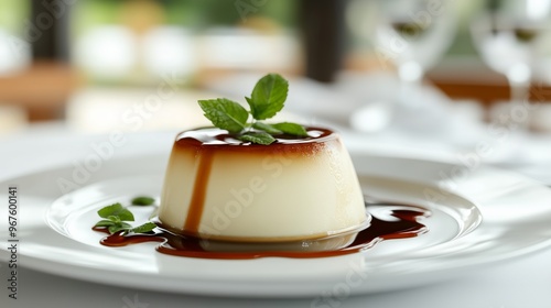 Delicious panna cotta dessert topped with caramel sauce and fresh mint leaves served on a white plate in a dining setting