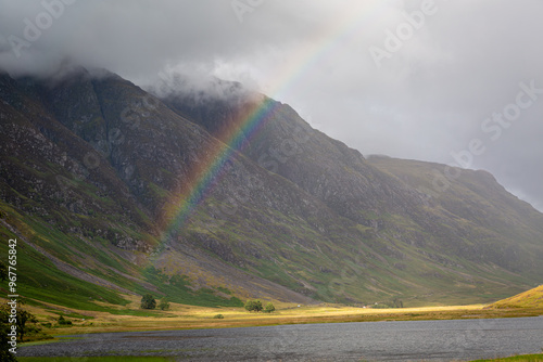 Loch Achtriochtan with a rainbow, Image shows the loch during a storm resulting in a rainbow across the water and dark clouds covering the sky and mountain peaks