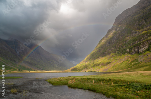 Loch Achtriochtan with a rainbow, Image shows the loch during a storm resulting in a rainbow across the water and dark clouds covering the sky and mountain peaks