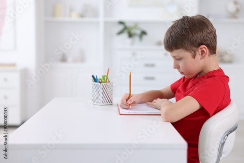 Boy with correct posture doing homework at white desk indoors