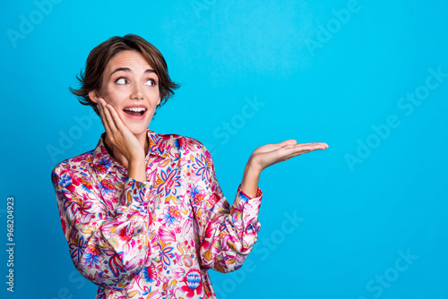 Photo of surprised lovely girl wear trendy clothes arm presents news benefit empty space isolated on blue color background