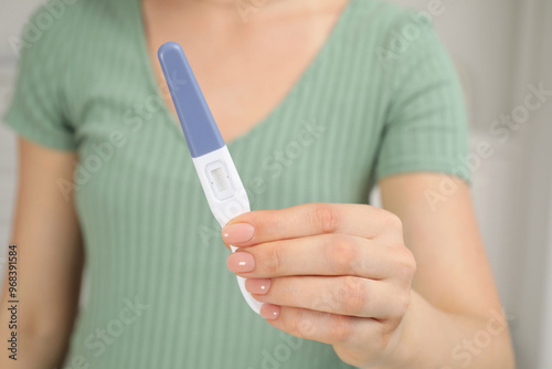 Woman holding pregnancy test indoors, closeup view