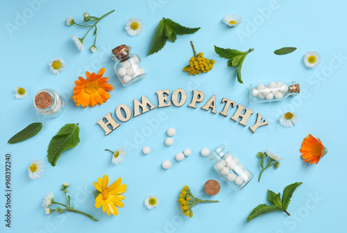 Word Homeopathy, pills and medicinal herbs on light blue background, flat lay