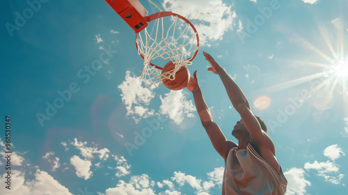 Young man dunking the ball in the hoop while playing basketball against the sky on a sunny day.