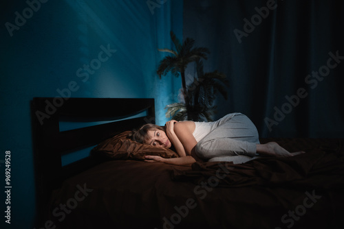 An elderly woman who woke up in the middle of the night from a nightmare or panic attack lies curled up on her bed in her bedroom, frightened