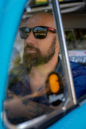 A bearded man in sunglasses inside a vintage car