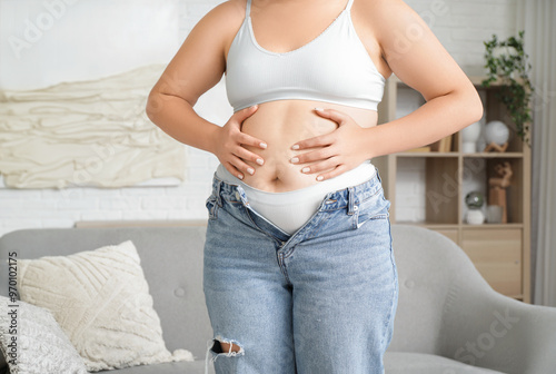 Overweight young woman touching her fat belly near mirror at home, closeup. Weight gain concept