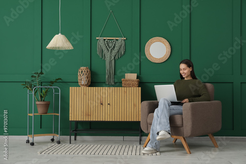 Young woman using laptop while sitting in armchair at home