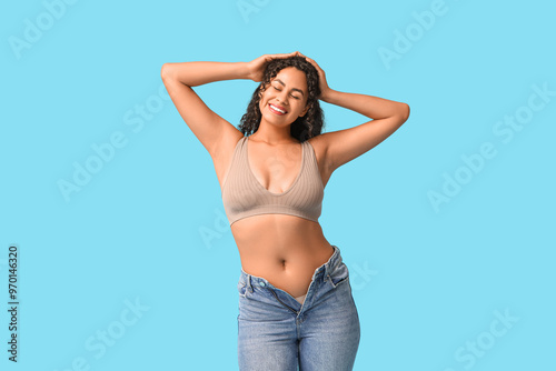 Beautiful young happy African-American body positive woman in tight jeans on blue background