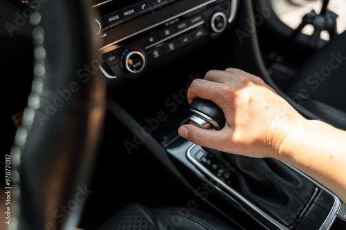 Driver hand rests on gear shift of automatic transmission in car on sunny day