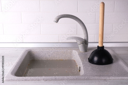 Clogged sink in the kitchen, plunger with wooden handle on the kitchen background, concept of removing the blockage