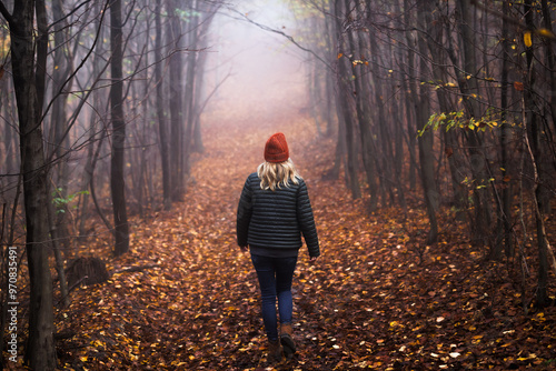 Lonely woman walks on footpath in dark foggy mystery forest. Spooky atmospheric mood in autumn woodland