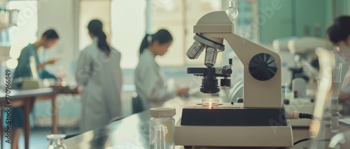 A busy laboratory where researchers in white coats focus intently on scientific experiments, with a microscope prominently in the foreground.