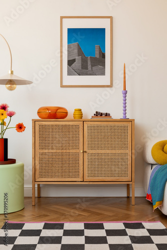 Fresh blooms in bright orange and yellow sit atop a wooden sideboard, framed by geometric decor and a retro glass dish, creating a cheerful modern space. Mock up.