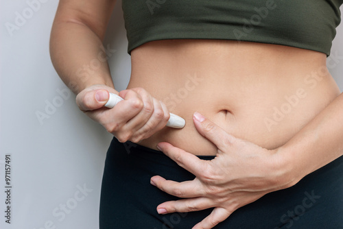 ng woman putting a hormonal injection in her stomach with pen syringe on a grey background. The use of lipolytics in cosmetology. Preparations for figure correction. Insulin injections for diabetes