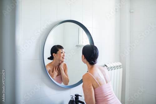 Woman doing skincare routine in front of bathroom mirror