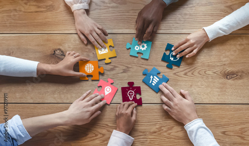 Hands of international coworkers sitting around table, putting colorful puzzles together, teamwork concept, top view