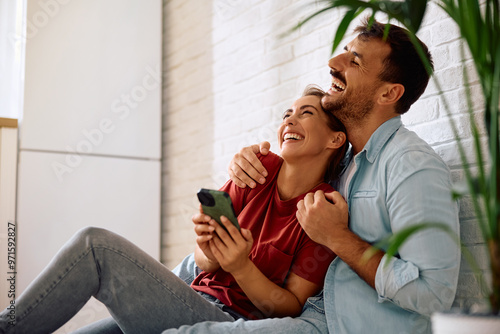 Cheerful couple using cell phone while relaxing at home.