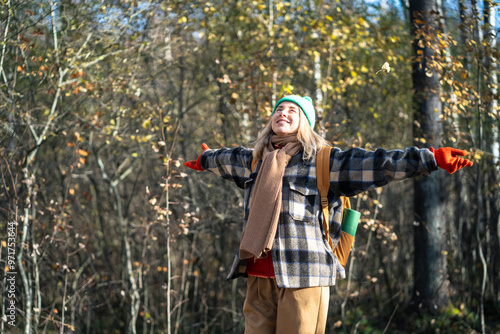 Joyful woman have trip with backpack raised arms feeling happiness, freedom in autumn forest basking in sunshine. Contented middle aged female traveler enjoys time alone walking in late fall woodland.