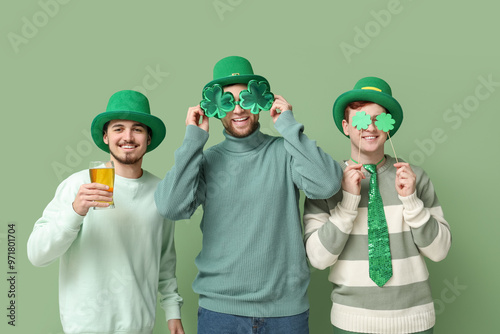 Happy young men in leprechaun's hats with beer, clovers and party glasses on green background. St. Patrick's Day celebration