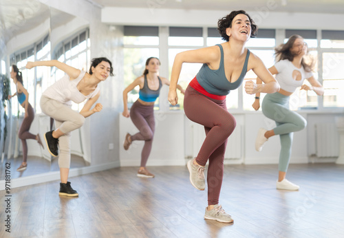 Expressive cheerful young Latina leading upbeat Zumba class for group of women in mirrored dance studio..